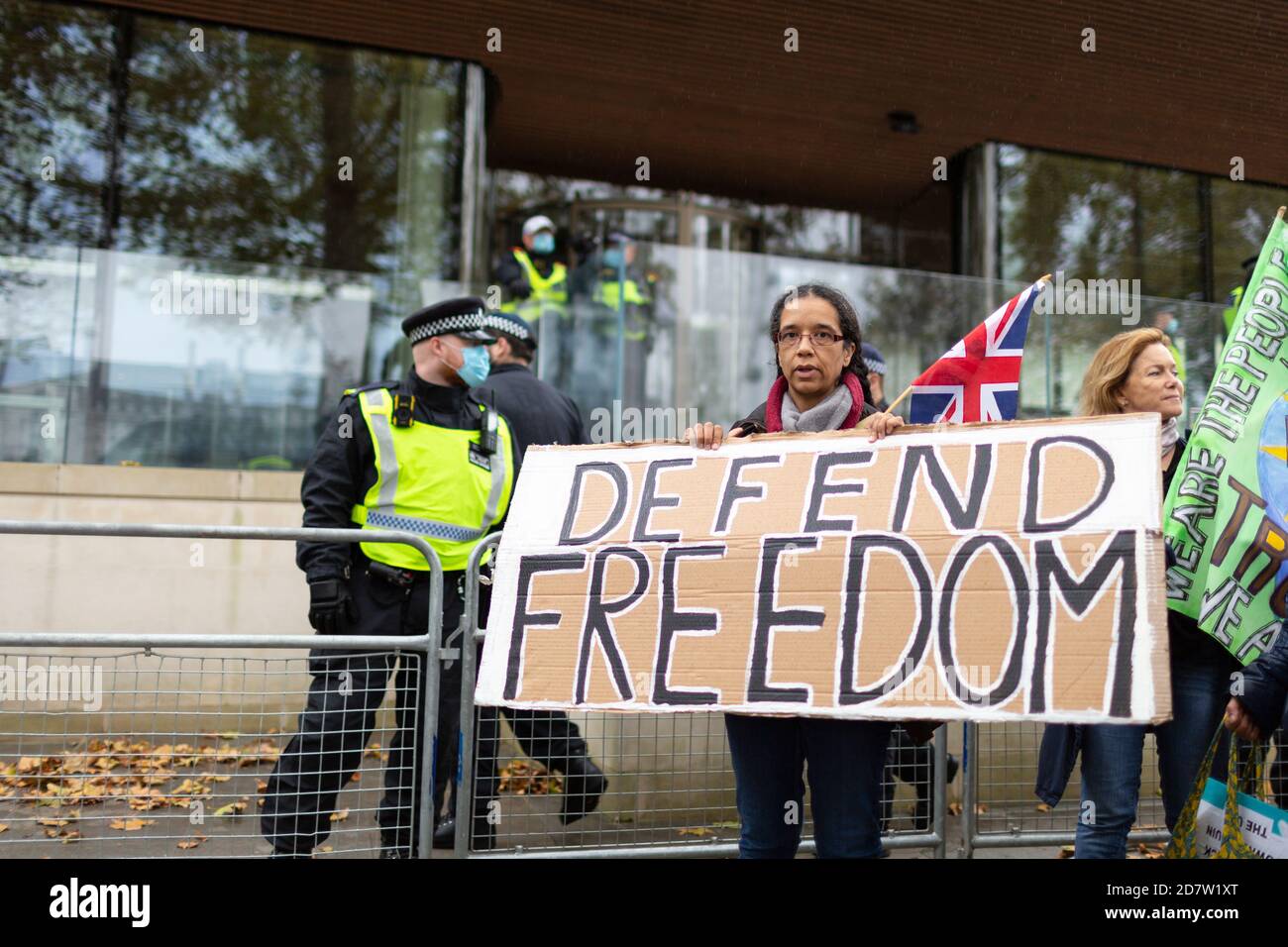 A protester holds a placard in front of police outside New Scotland Yard during an anti-lockdown rally in London, 24 October 2020 Stock Photo