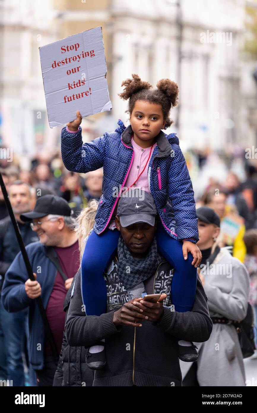A child with protest placard rides piggyback during an anti-lockdown rally in London, 24 October 2020 Stock Photo