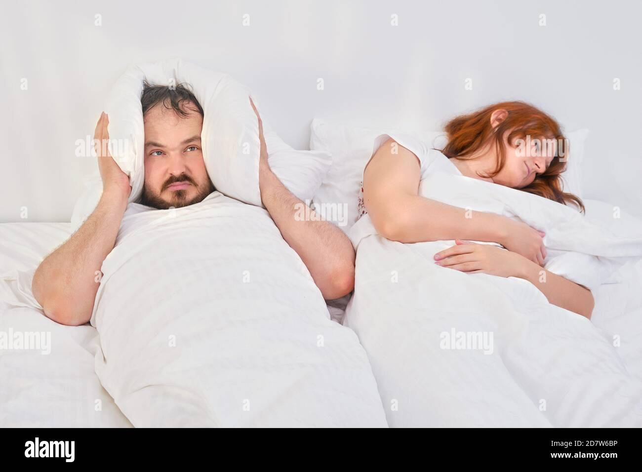 The man covered his head with a pillow due to his wife's snoring. Trouble sleeping in the family. Relationship problems coupled with isolation due to Stock Photo