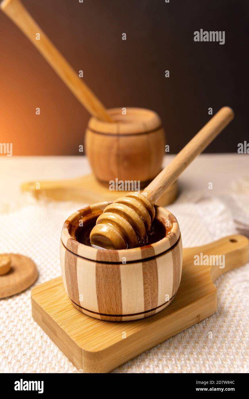 wooden stick to bowl with liquid floral fresh honey. Healthy organic honey dripping, pouring from honey wooden spoon. Stock Photo
