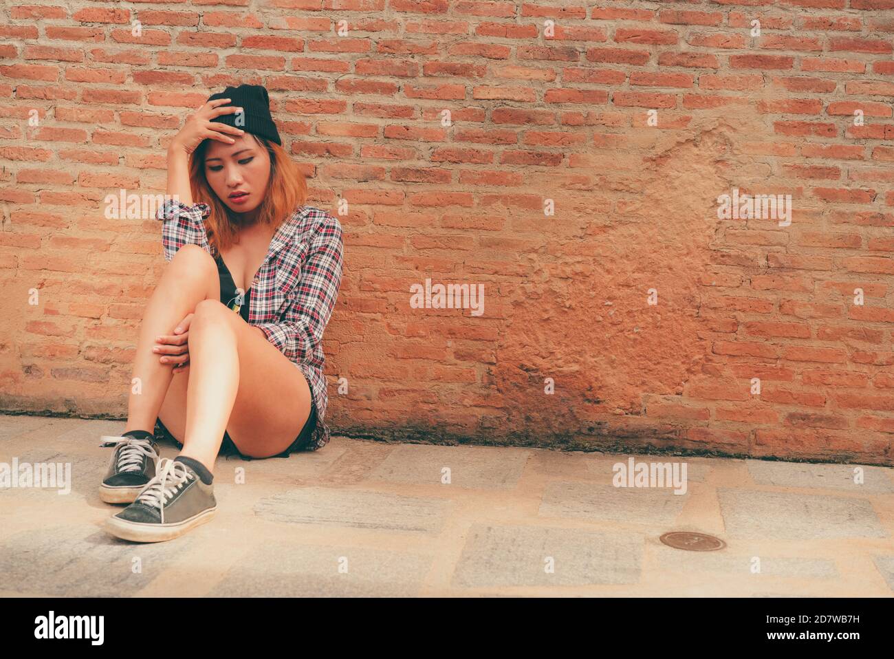 Depressed teenage woman feeling sad alone against brick wall in old town. Education and family failure concept. Stock Photo