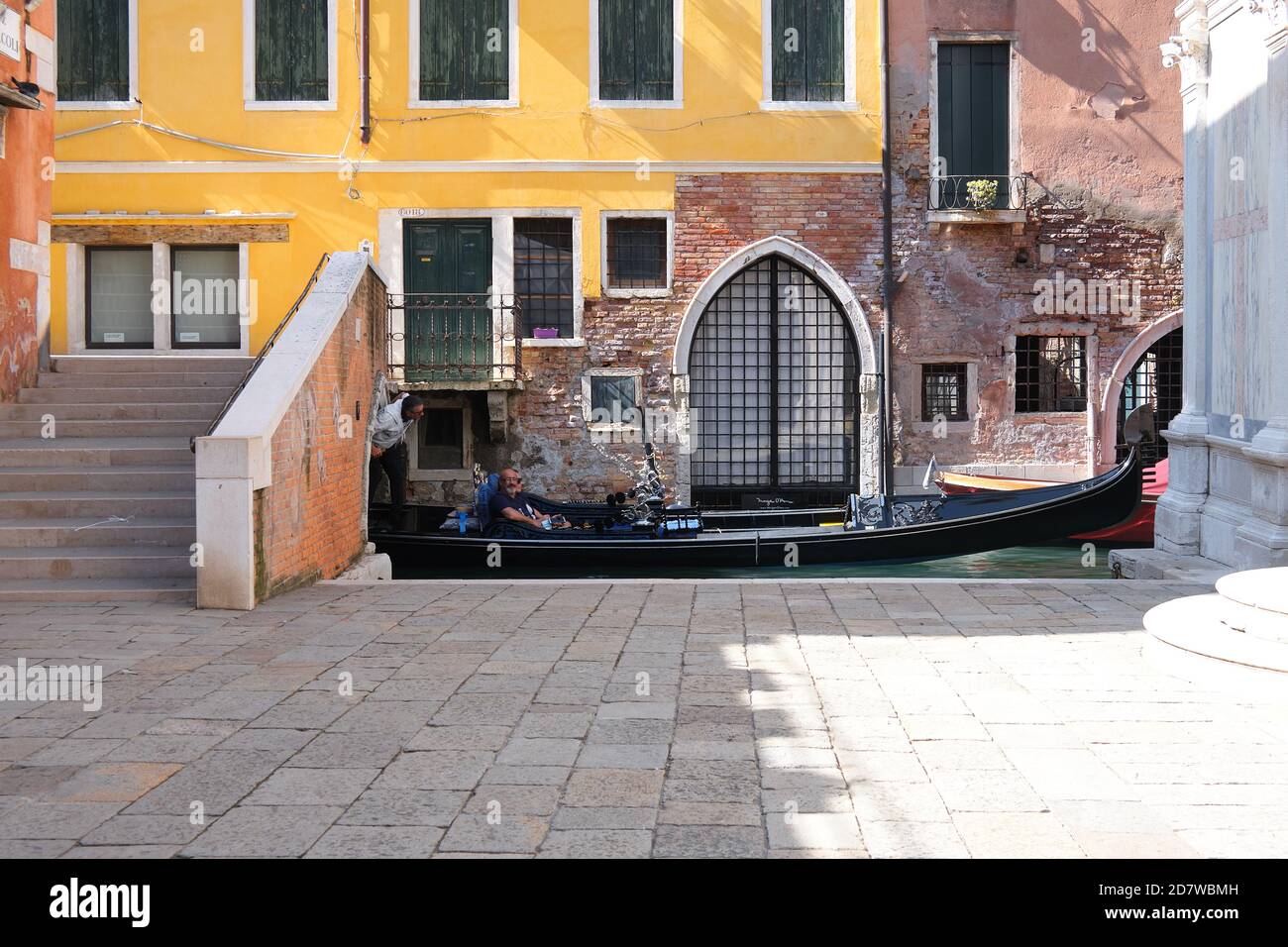 Romantic old houses. Gondola passes under pedestrian bridge across canal. Hardly anybody outdoors. Tourists are returning to Venice, but far fewer Stock Photo