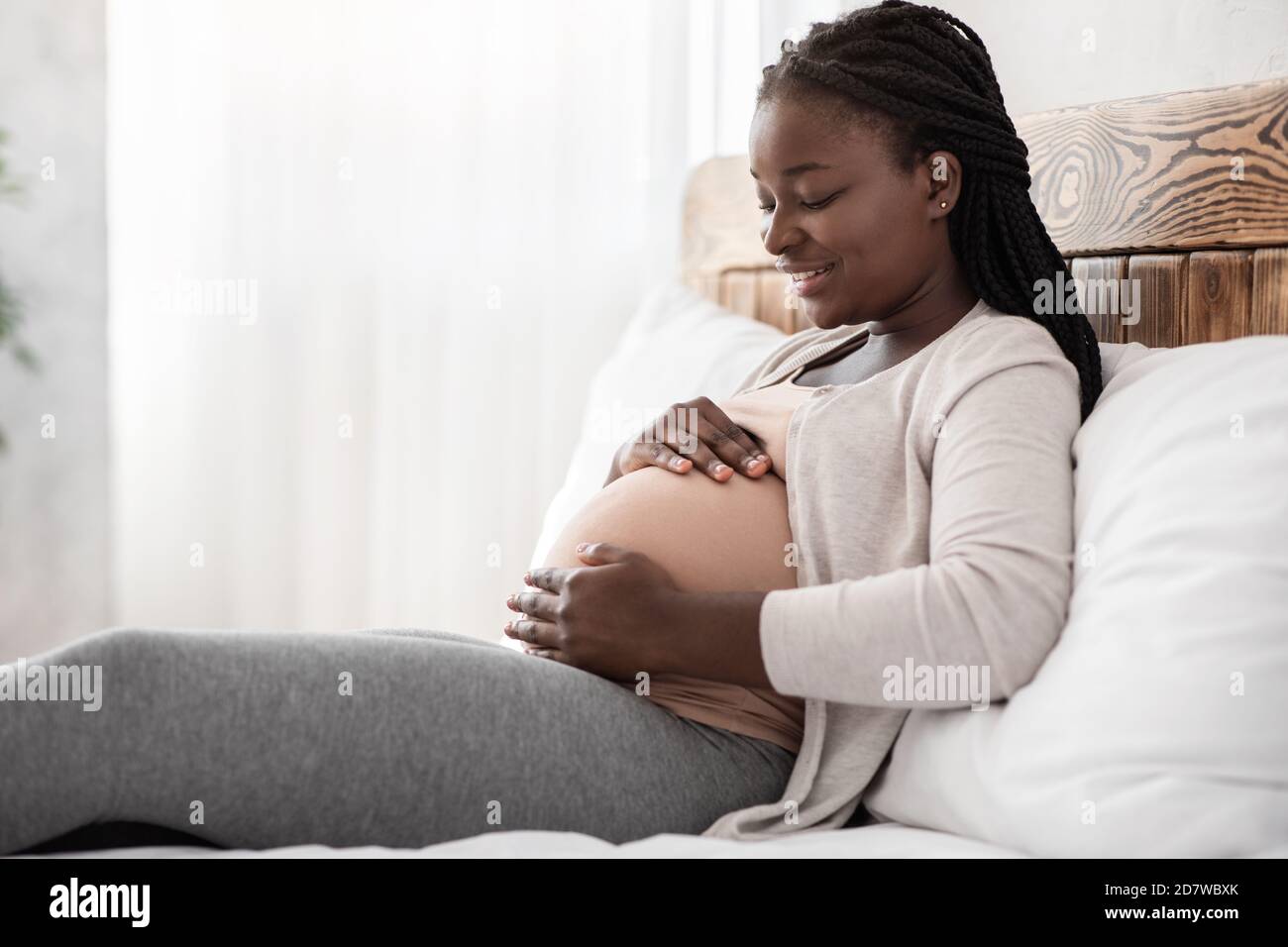 Desirable Pregnancy. Black Pregnant Woman Relaxing On Bed At Home, Touching Belly Stock Photo