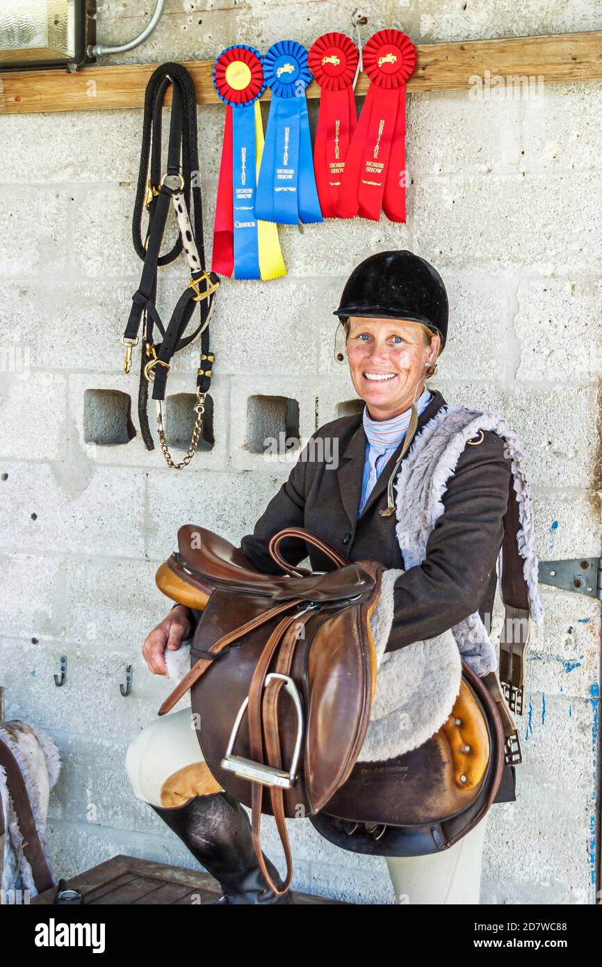 Miami Florida,Tropical Park,Heritage Horse Show,woman female rider holds holding saddle riding tack gear,stable stables winning ribbons blue red, Stock Photo