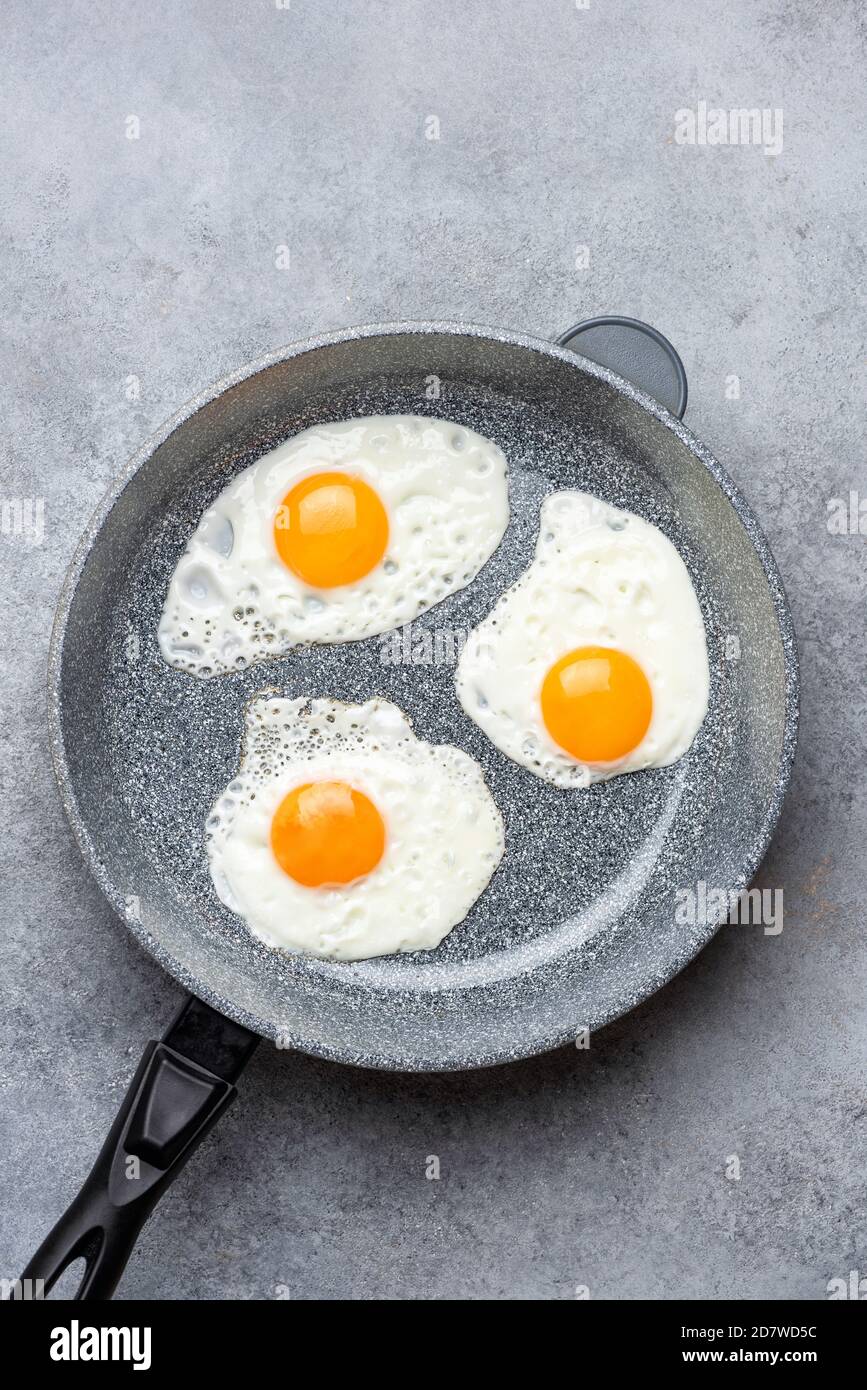 Three sunny side up eggs in skillet isolated on grey concrete background, top view with copy space for design or text Stock Photo