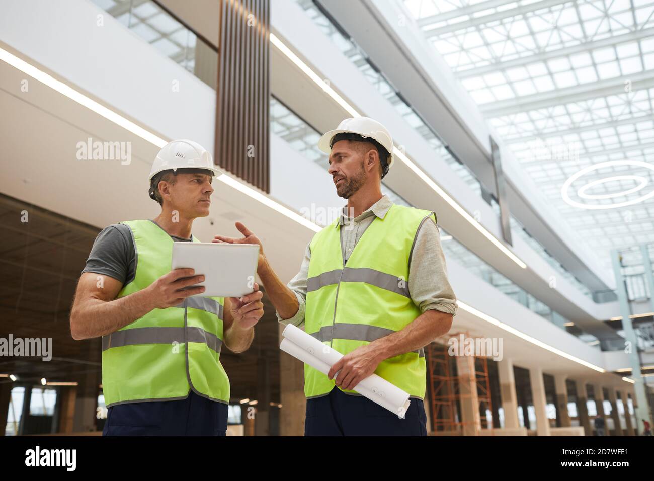 Low angle portrait of two professional building contractors using digital tablet while standing at construction site in office building, copy space Stock Photo