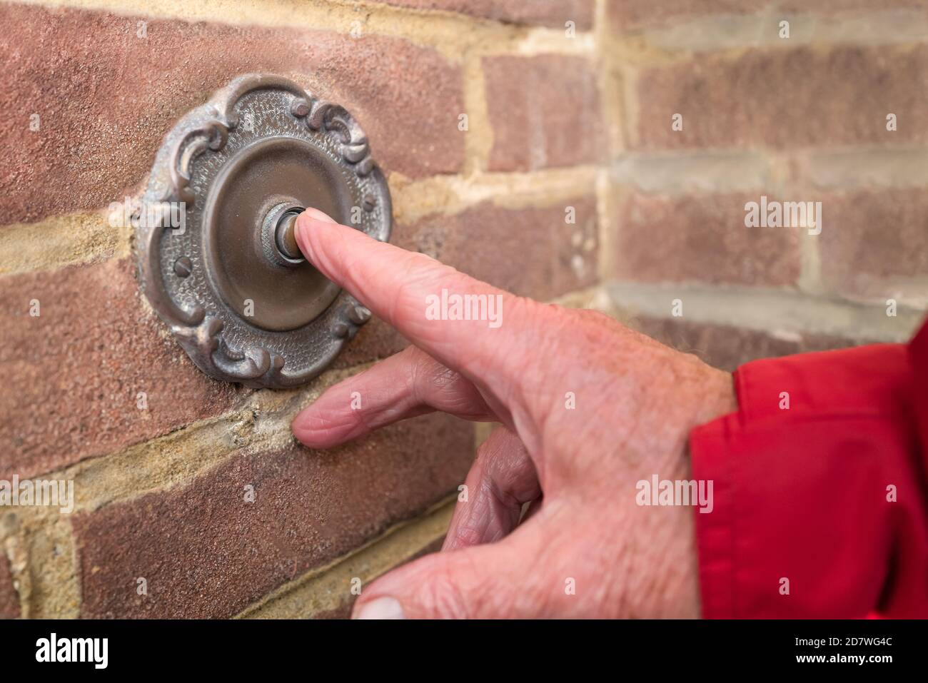 A vintage antique style metal door bell being pushed by a male hand iwith a red sleeve Stock Photo
