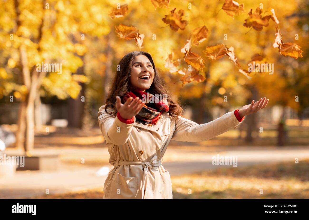 Joyful young woman in autumn outfit catching yellow leaves during her walk at park on bright fall day Stock Photo
