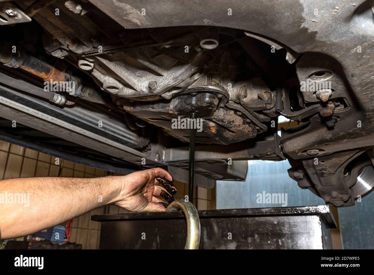 Draining used diesel engine oil from an oil pan into a metal container in a car workshop, visible dirty hands of a mechanic. Stock Photo