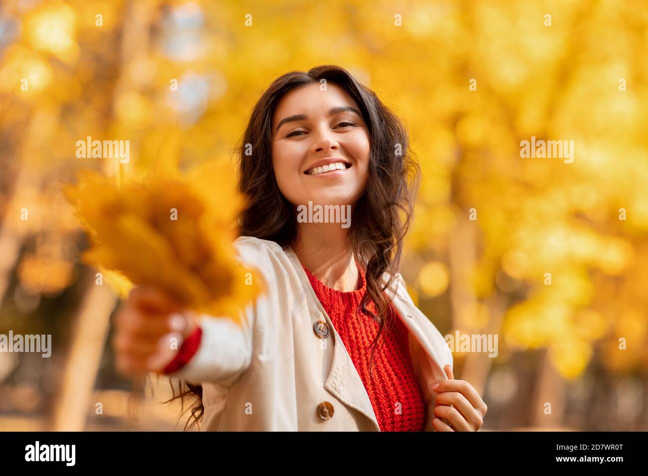 Lovely young woman handing bouquet of yellow autumn leaves to camera on walk at park Stock Photo