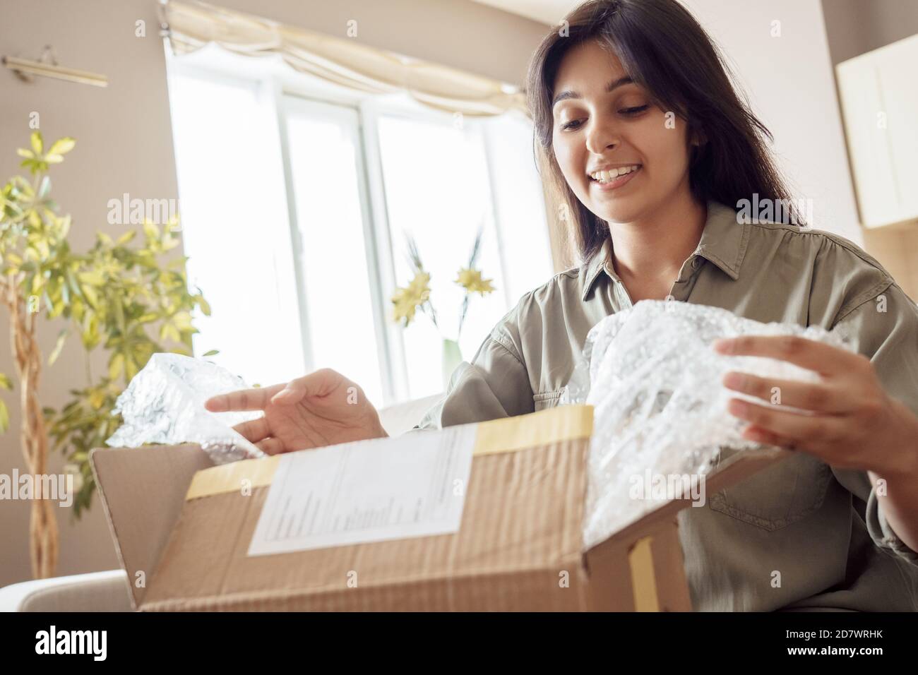 Smiling indian woman shopper customer opening post parcel box at home. Stock Photo