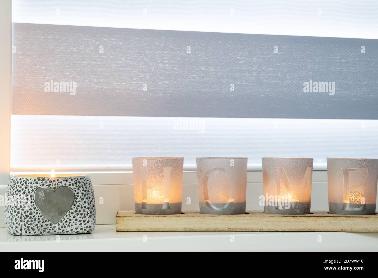 candles with the inscription HOME on the windowsill with beautiful blinds Stock Photo