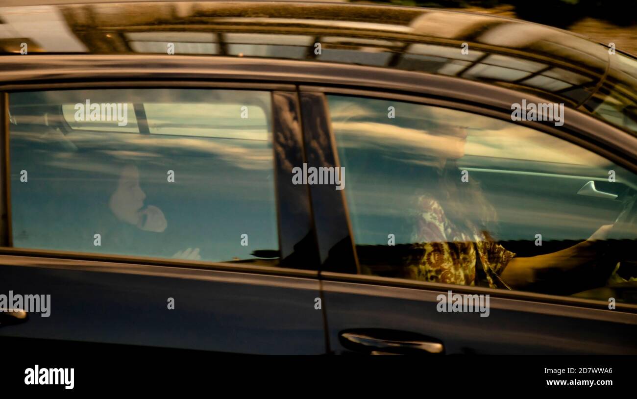 Belgrade, Serbia - October 02, 2020: Woman driving a car and a little girl riding on a back seat of it, through window with reflections and blurs Stock Photo