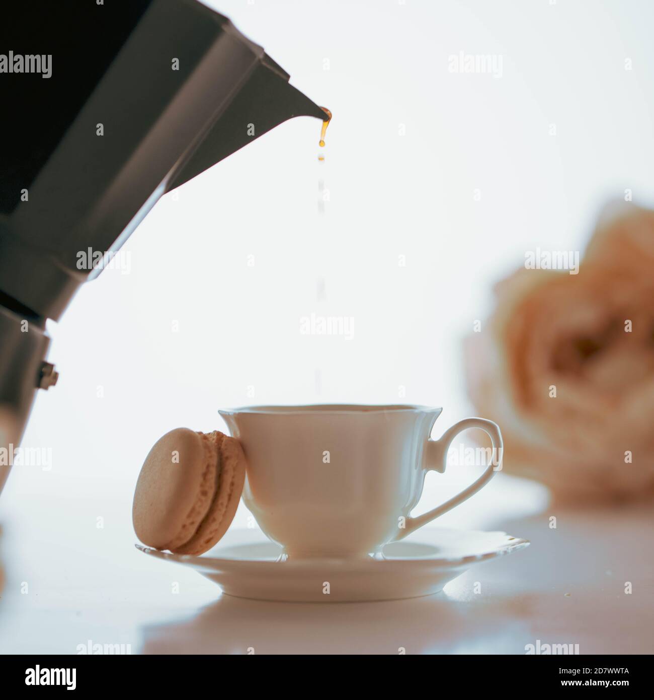Coffee pouring to a white porcelain cup with a macaron from a black coffeemaker Stock Photo