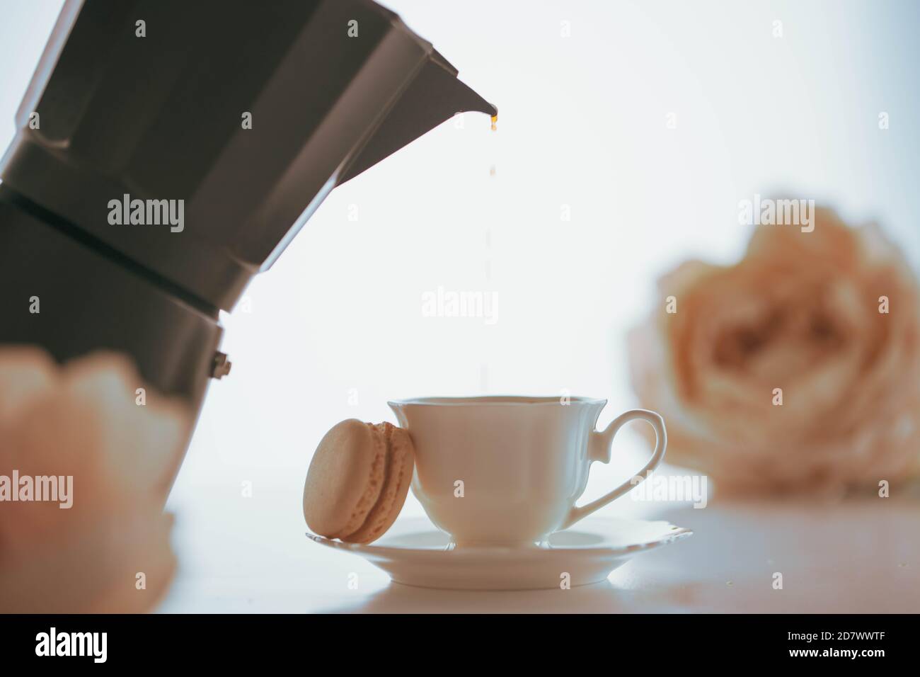 Coffee pouring to a white porcelain cup with a macaron from a black coffeemaker Stock Photo
