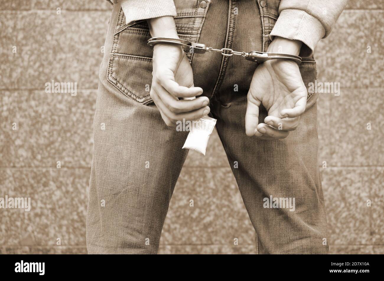 Arrested drug dealer in handcuffs with small heroin drug package on dark wall background. Illegal drug trafficking concept Stock Photo