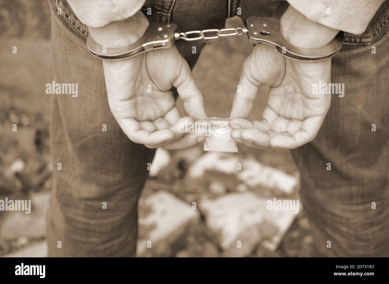 Arrested drug dealer in handcuffs with small heroin drug package on dark wall background. Illegal drug trafficking concept Stock Photo