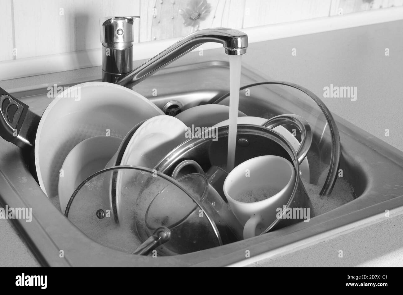Dirty dishes and unwashed kitchen appliances lie in foam water under a