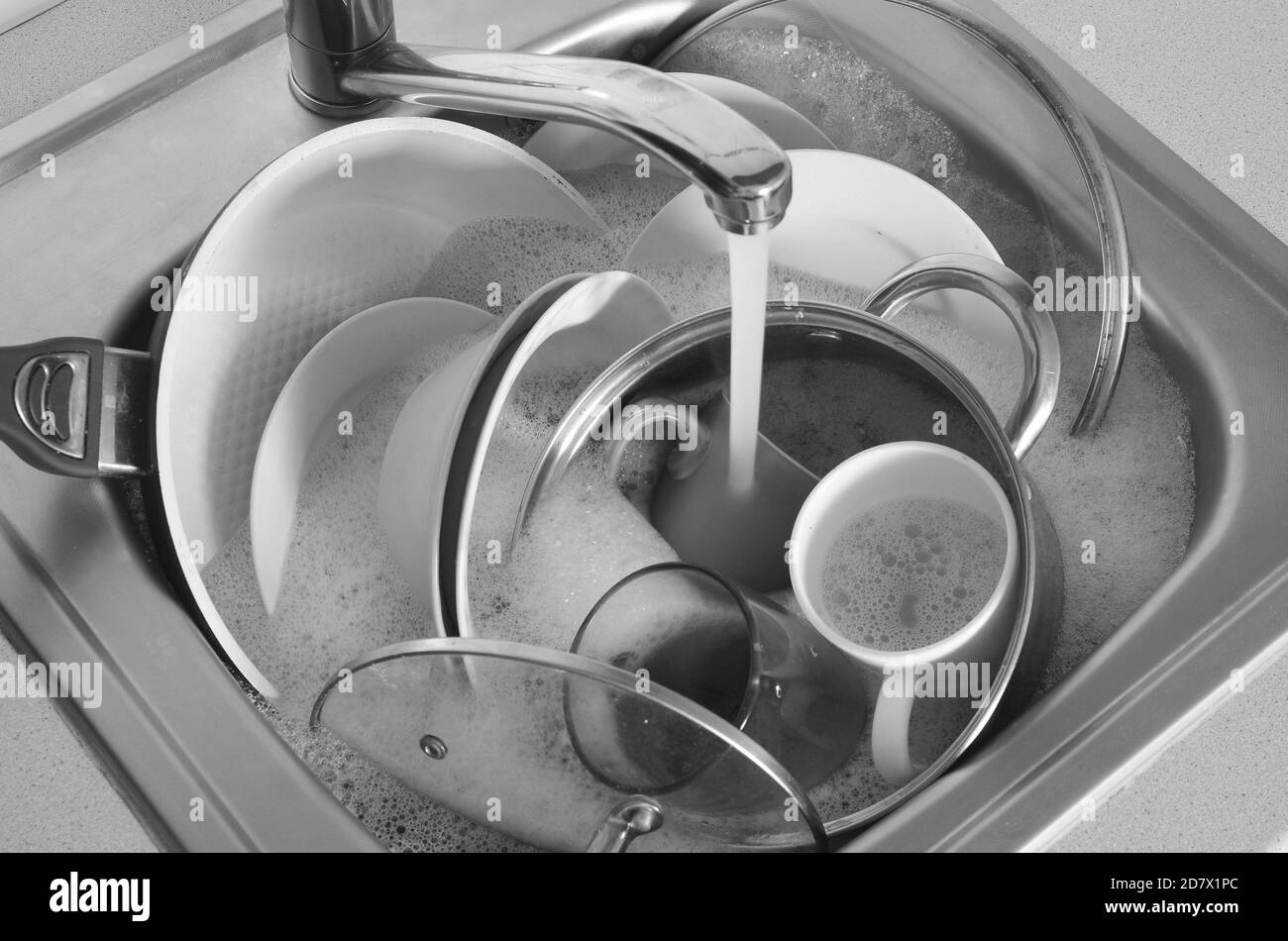 Dirty dishes and unwashed kitchen appliances lie in foam water under a
