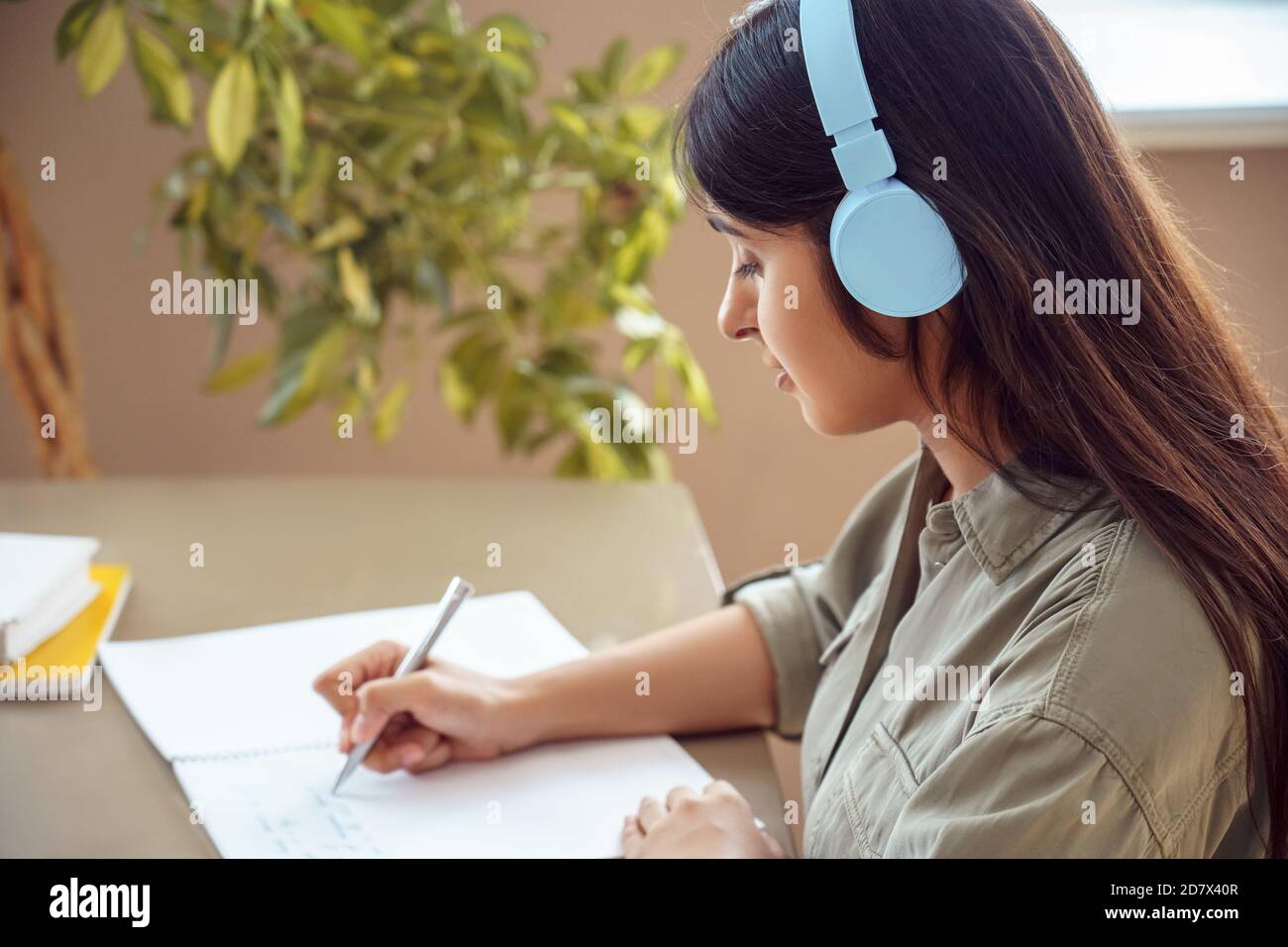 Indian woman student wearing headphones writing listening audio course at home. Stock Photo