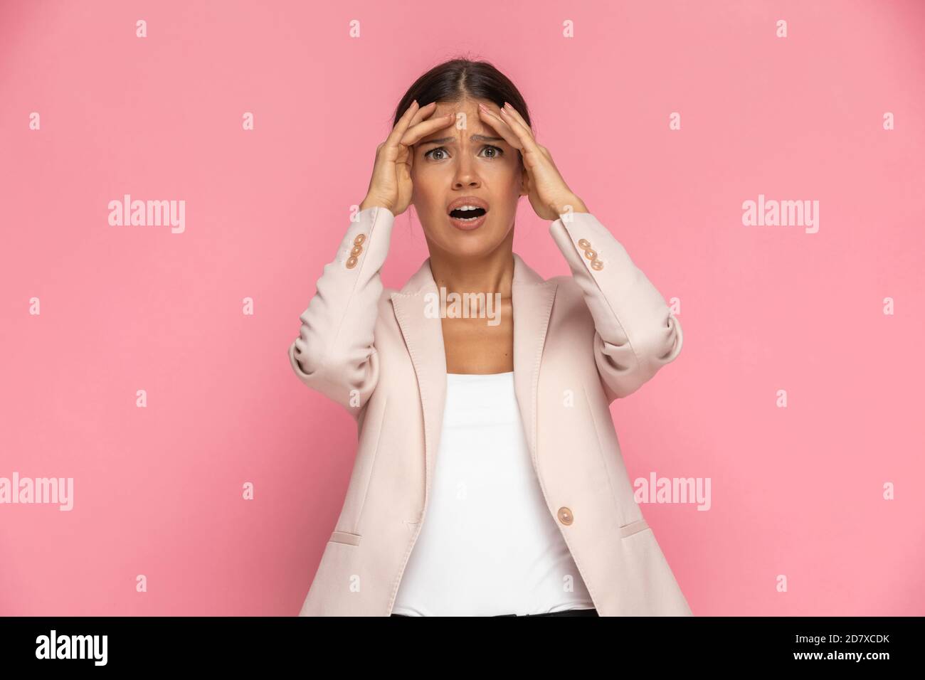 beautiful smart casual woman is looking at the camera and feeling shocked, slapping her head against pink background Stock Photo