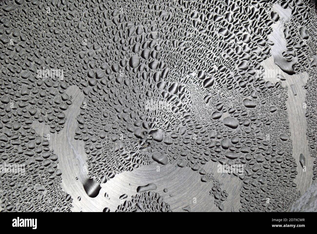 Water droplets of various shapes and sizes on a metallic surface Stock