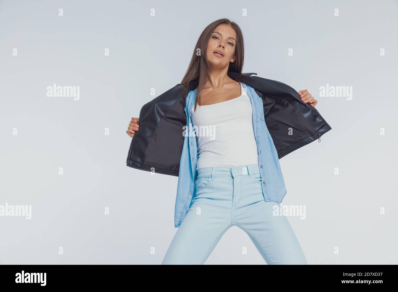 Determined fashion model taking off her leather jacket, standing on ...