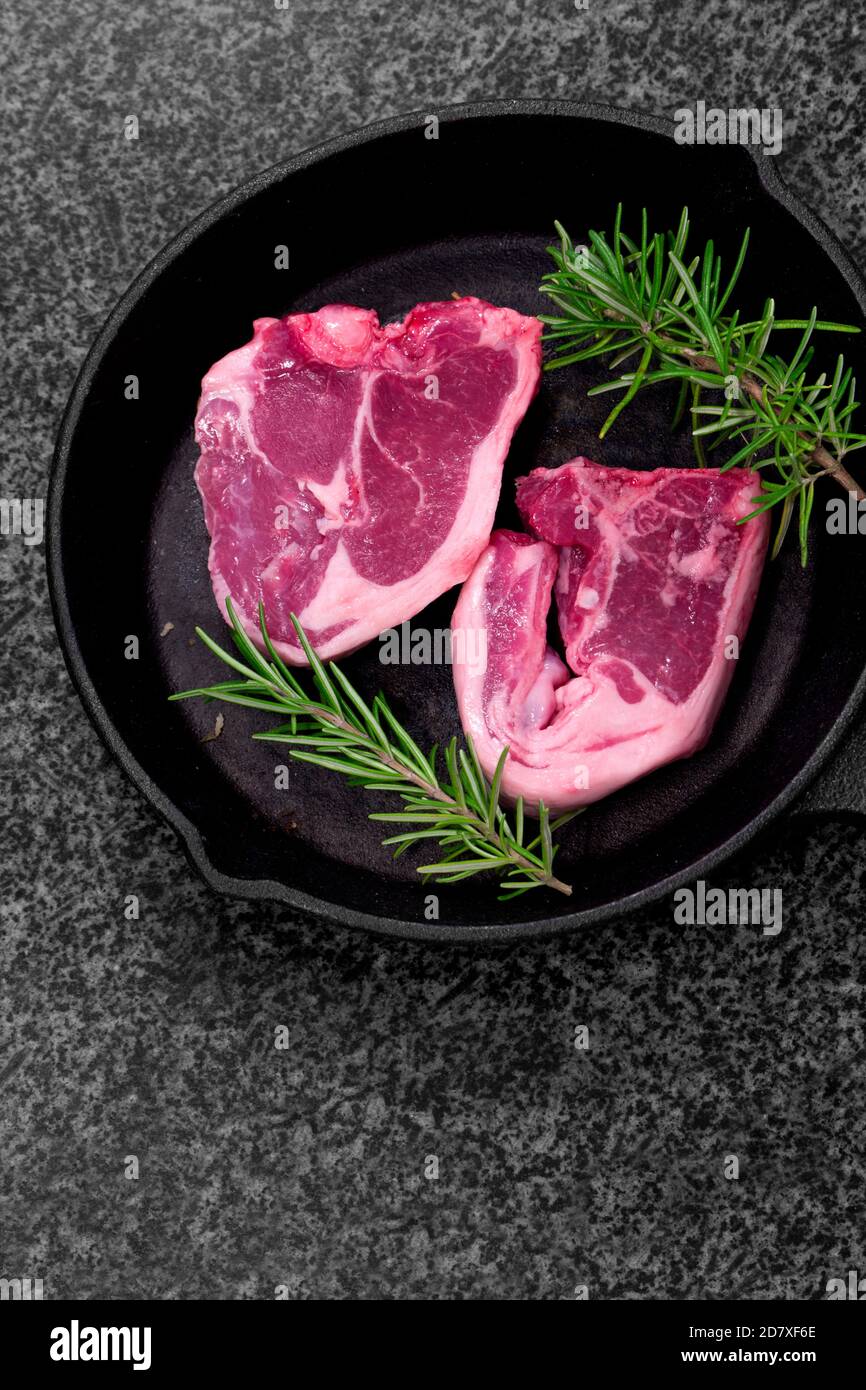 Lamb loin chops with rosemary in a cast iron frying pan. On a black granite background Stock Photo