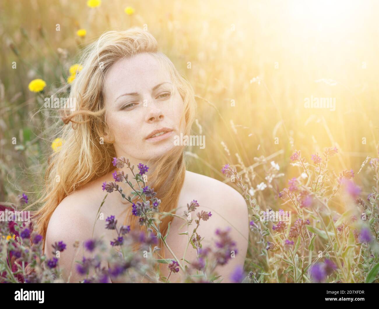 Artistic portrait of freckled woman on natural background. Young woman enjoying nature among the flowers and grass. Close up summer portrait Stock Photo