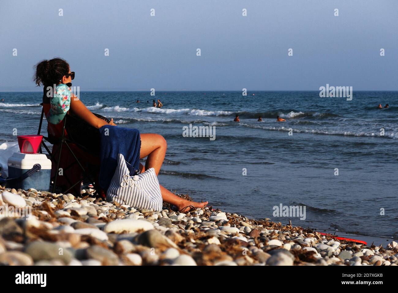 Woman sitting on a chair on the beach looking towards the sea Stock Photo
