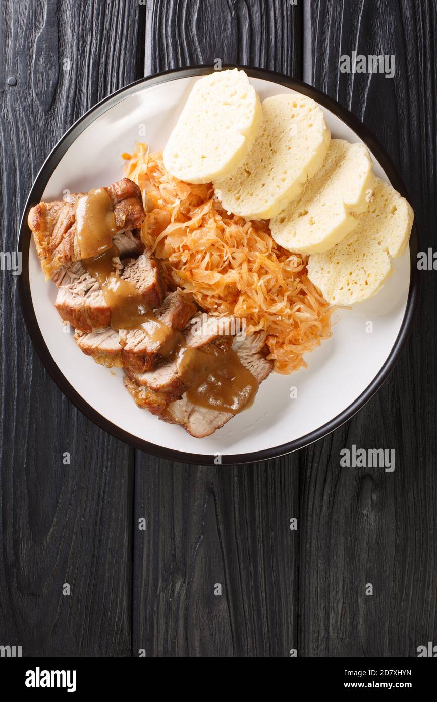 Roasted pork with stewed sauerkraut and dumplings close-up in a plate on the table. Vertical top view from above Stock Photo