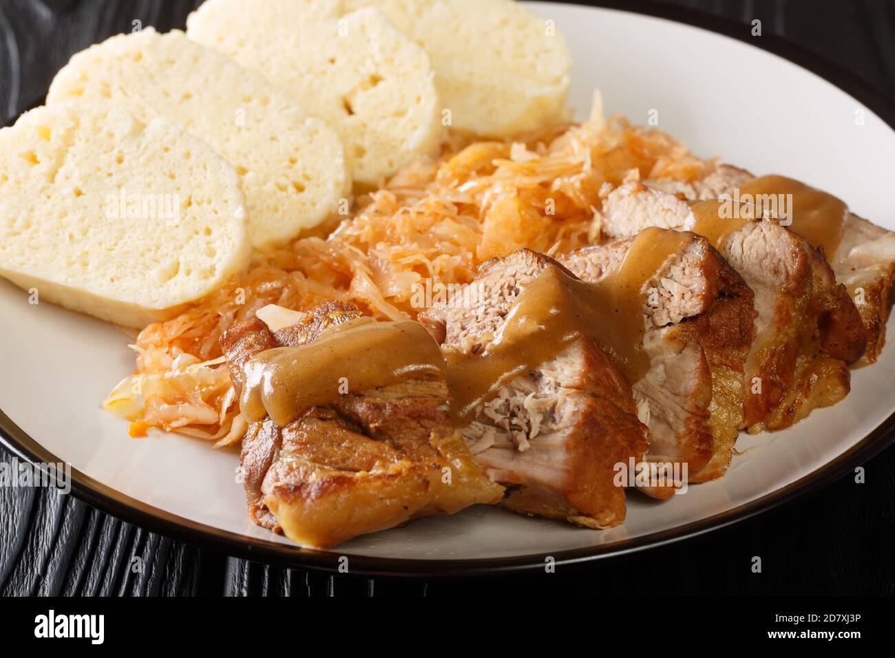 Vepro knedlo zelo this is a Czech dish consisting to pork, dumplings and cabbage close-up in a plate on the table. Horizontal Stock Photo