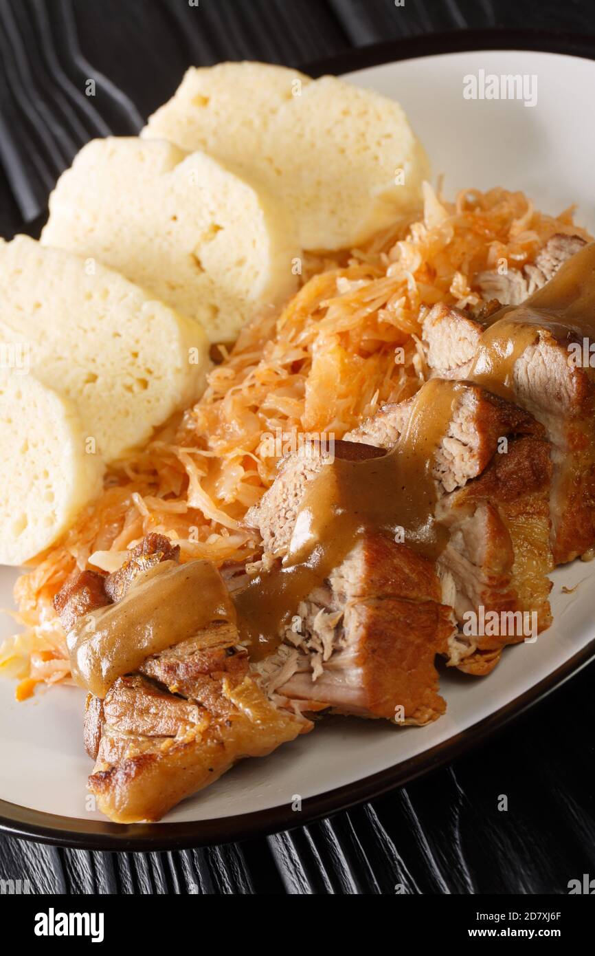 Roasted Pork, Dumplings and Sauerkraut Vepro knedlo zelo close-up in a plate on the table. Vertical Stock Photo