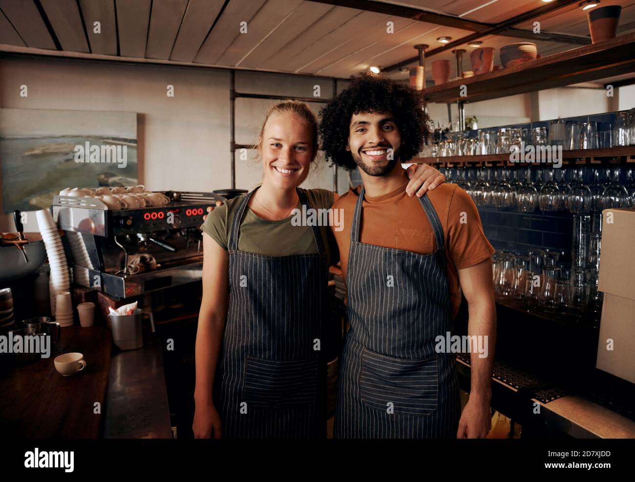 Young cafe owners wearing apron standing behind counter in cafe looking at camera Stock Photo