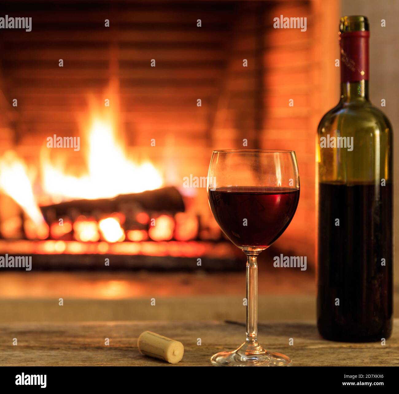 Glass of red wine and a bottle on burning fireplace background. Warm