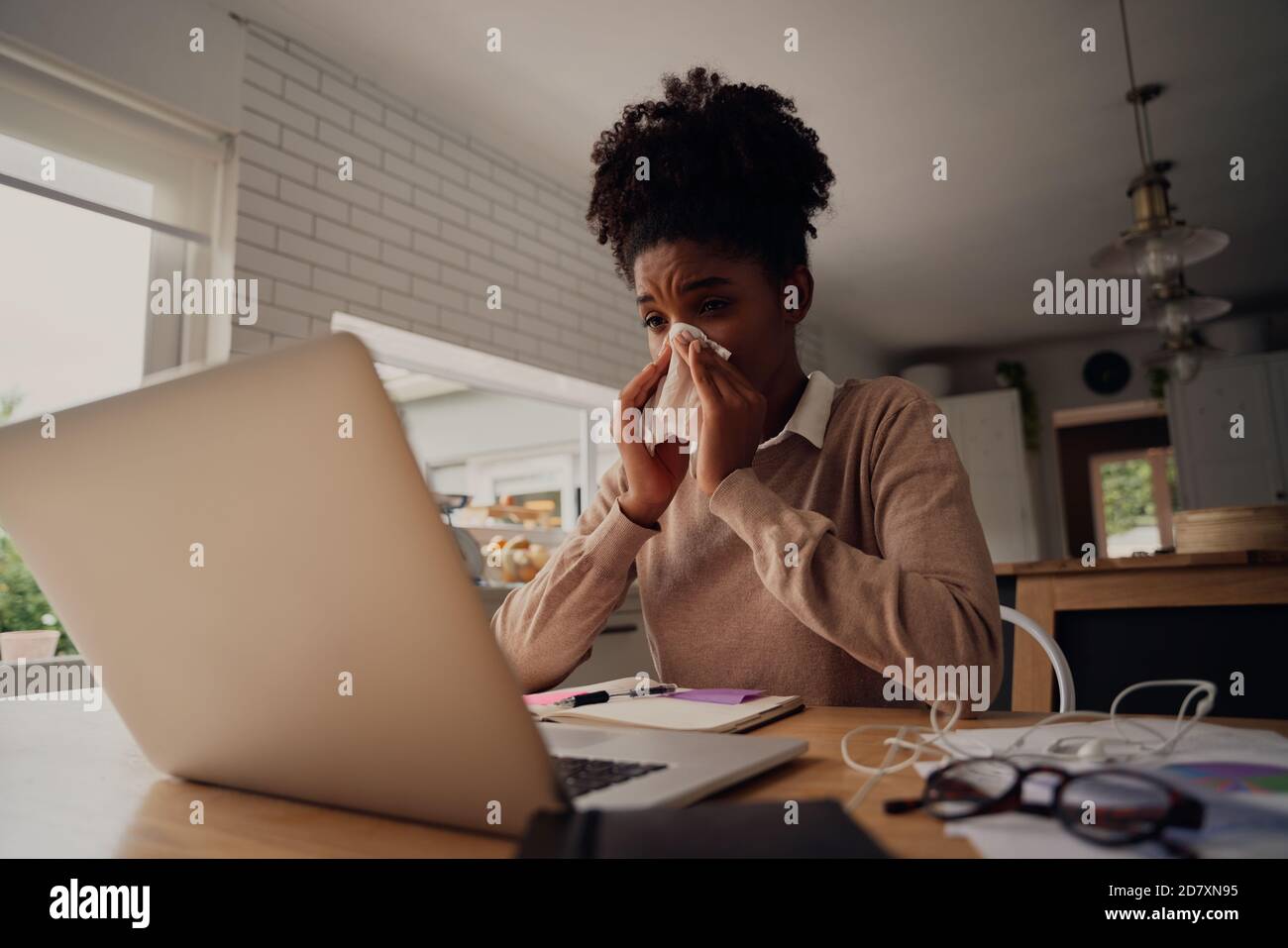Sick woman working from home while blowing nose due to virus with cold and cough Stock Photo