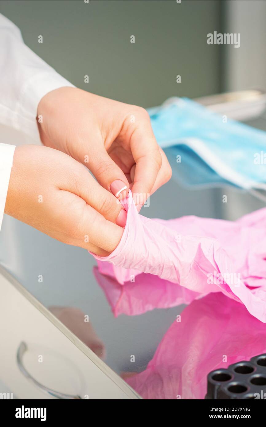 Nurse's hands putting on pink sterilized protective gloves in the