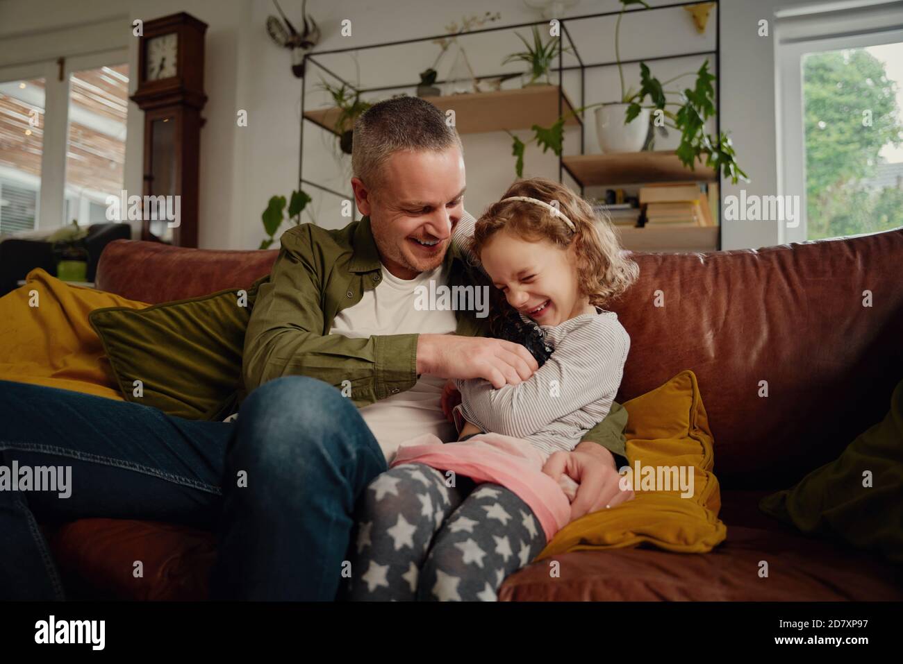 Playful father and daughter tickling each other while relaxing on sofa at home Stock Photo