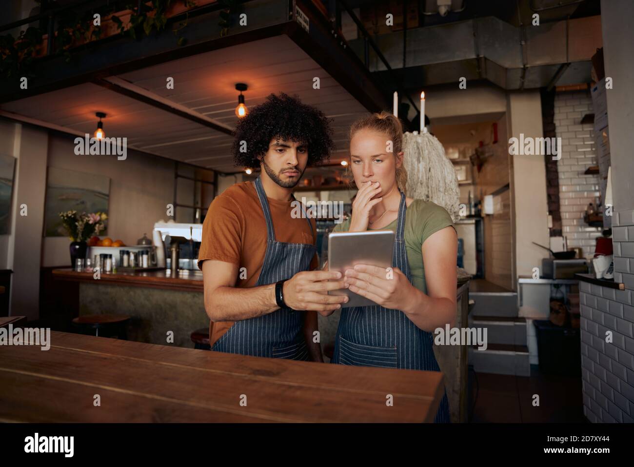Young serious co-workers using digital tablet while standing in modern cafe Stock Photo