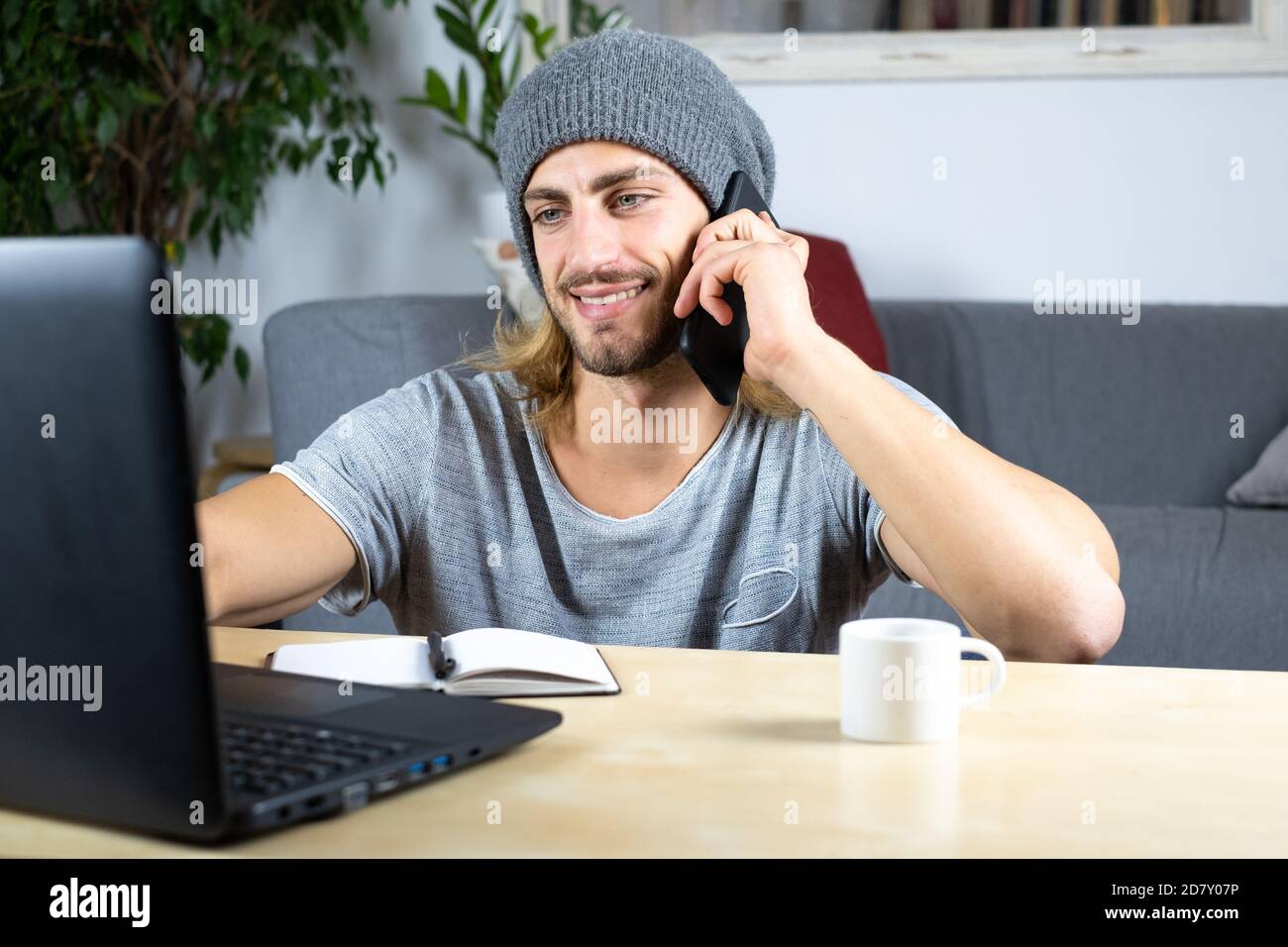 Handsome young caucasian man using computer working at home and talking with mobile feeling happy with smile showing teeth Stock Photo