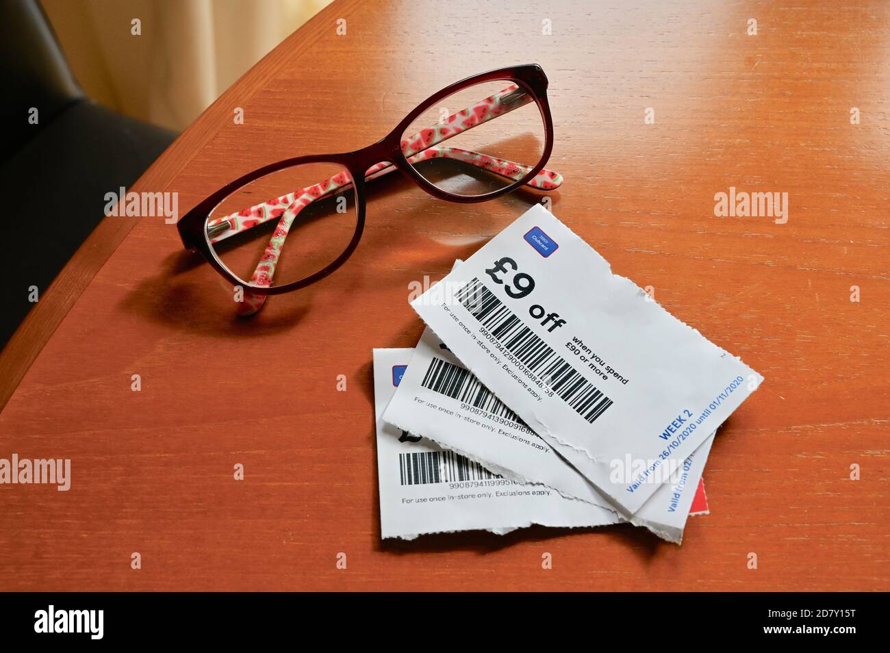 Tesco money saving vouchers left on the table with a pair of glasses. Stock Photo