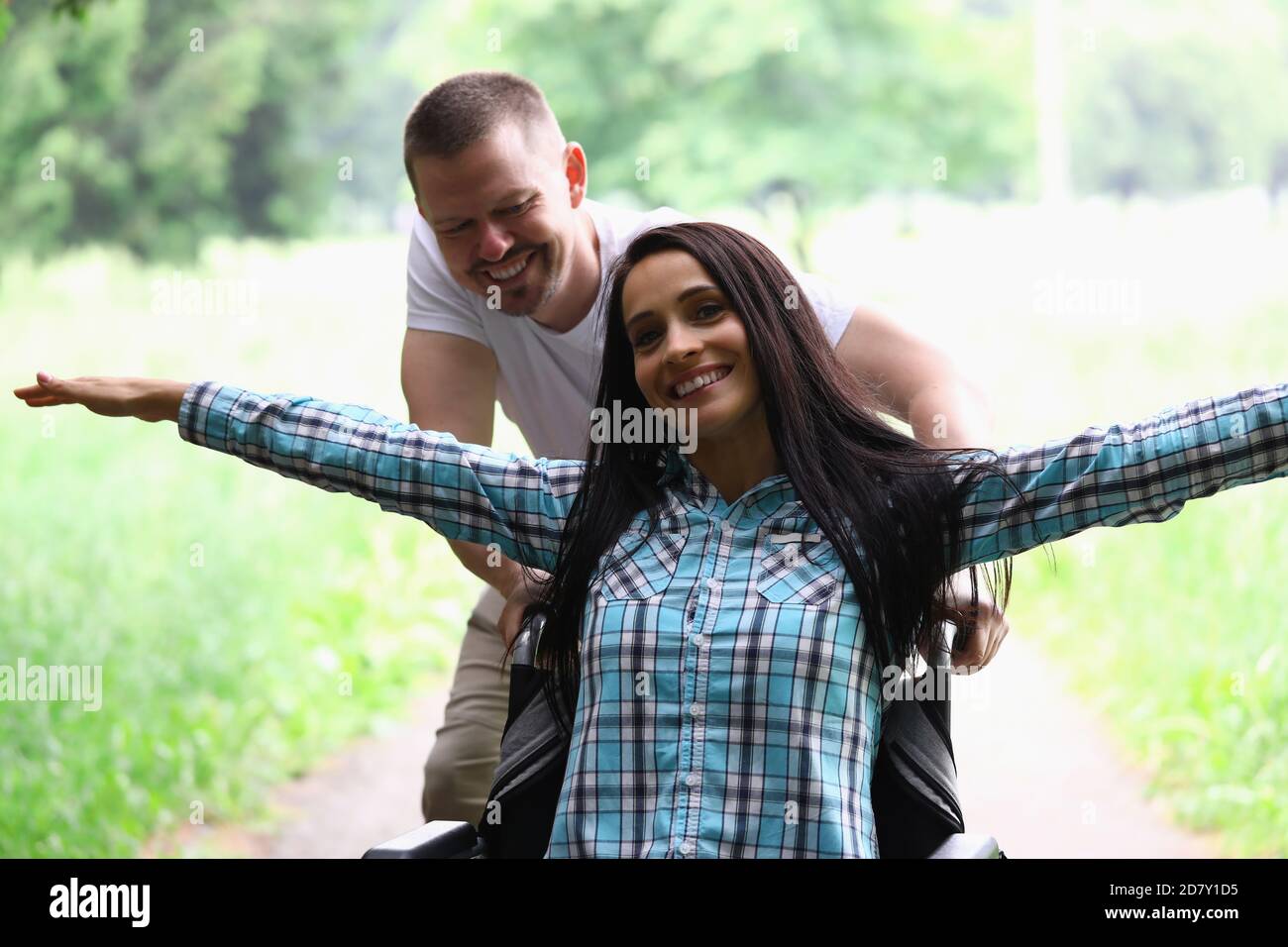 Woman is sitting in wheelchair smiling with her arms spread out man is rolling. Stock Photo