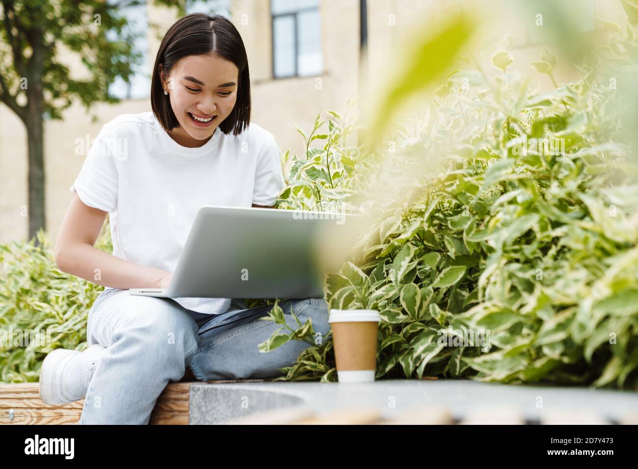 Photo of cheerful young asian woman sitting outdoors using laptop ...