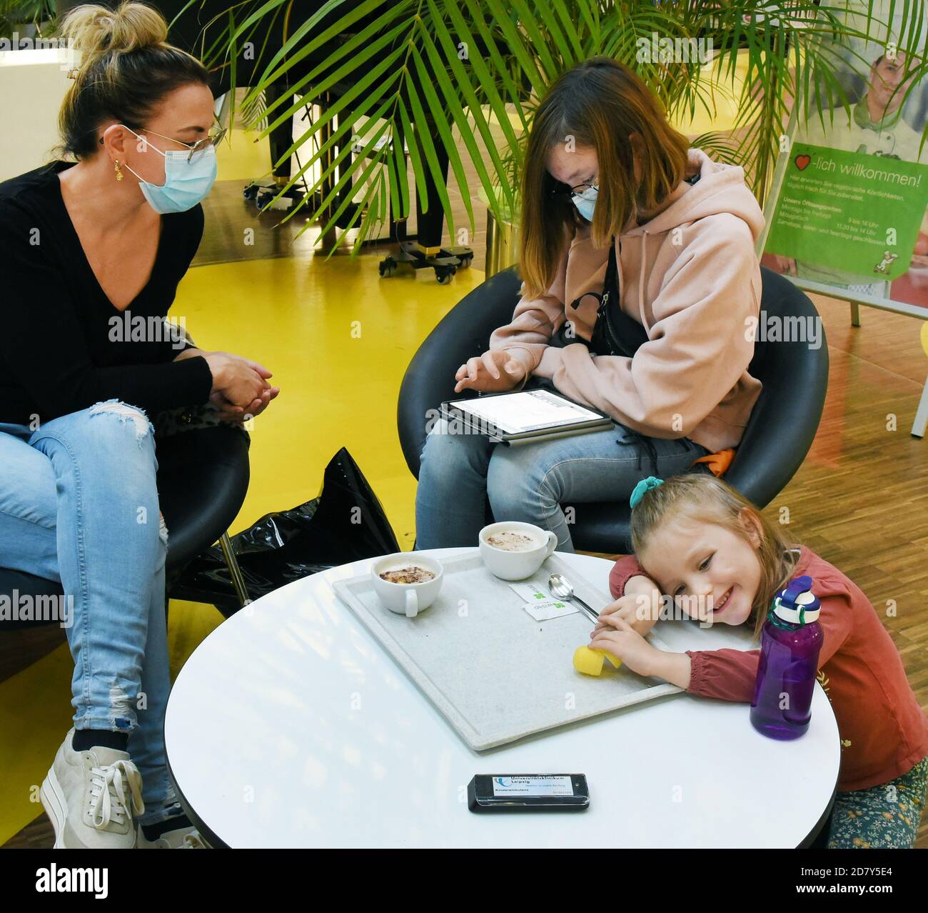 23 October 2020, Saxony-Anhalt, Köthen: A mother sits with her two children in the children's hospital of the University Hospital relaxed at a table in the cafeteria, on which a pager (pager receiver, in the foreground) is located, which signals the call to the consulting room with a buzzing sound. In the current time with increasing corona numbers, the new paging system, with which patients can move up to 500 meters away, is intended to equalize the situation in the waiting areas. The pagers should make it possible to maintain the distances even in the case of a large crowd. The paging receiv Stock Photo