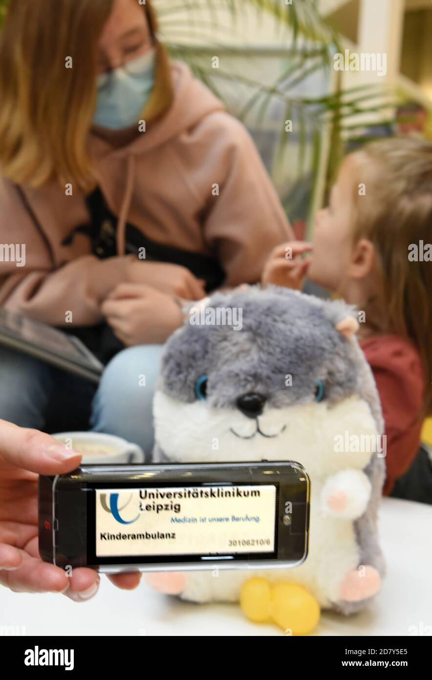 23 October 2020, Saxony-Anhalt, Köthen: In the pediatric clinic of the University Hospital, a mother sitting with her two children at a table in the cafeteria holds a pager (pager receiver) in her hand. With a buzzing sound the pager signals the call to the consulting room. In the current time with increasing corona numbers, the new paging system, which allows patients to move up to 500 meters away, is intended to equalize the situation in the waiting areas. The pagers should make it possible to maintain the distances even in the case of a large crowd. The paging receivers are currently being Stock Photo