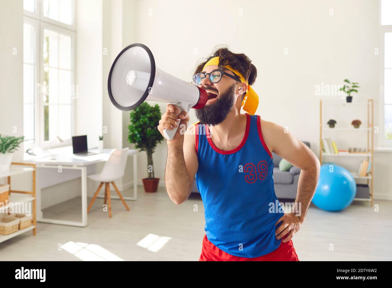 Funny bearded male trainer loudly shouts into a loudspeaker urging everyone to do exercises. Stock Photo