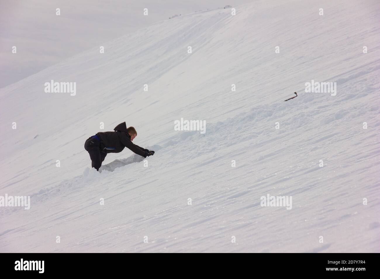 A young boy mountaineer digging in the snow with a shovel to perform