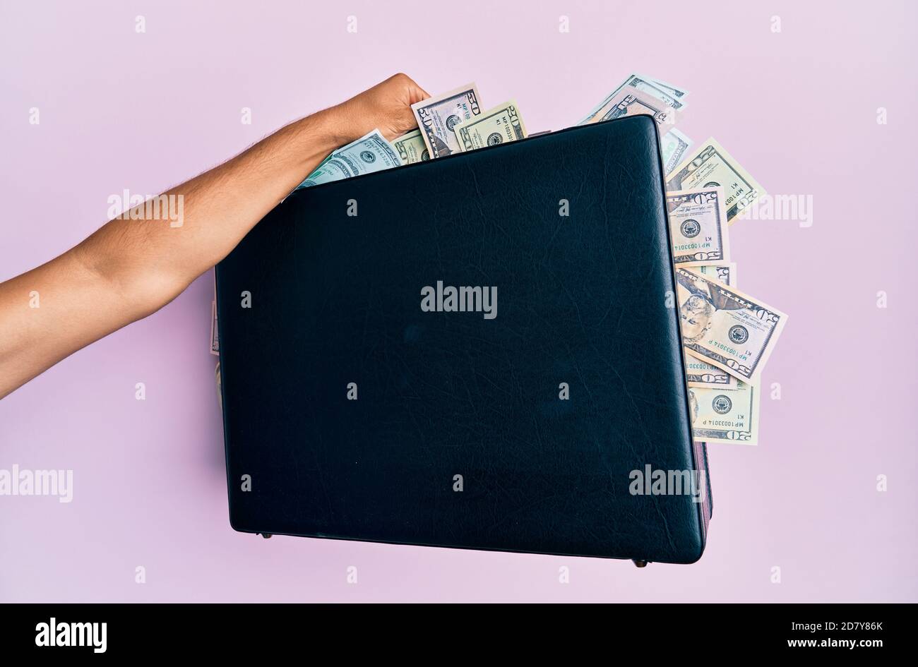 Hand of hispanic man holding briefcase with dollars over isolated pink background. Stock Photo