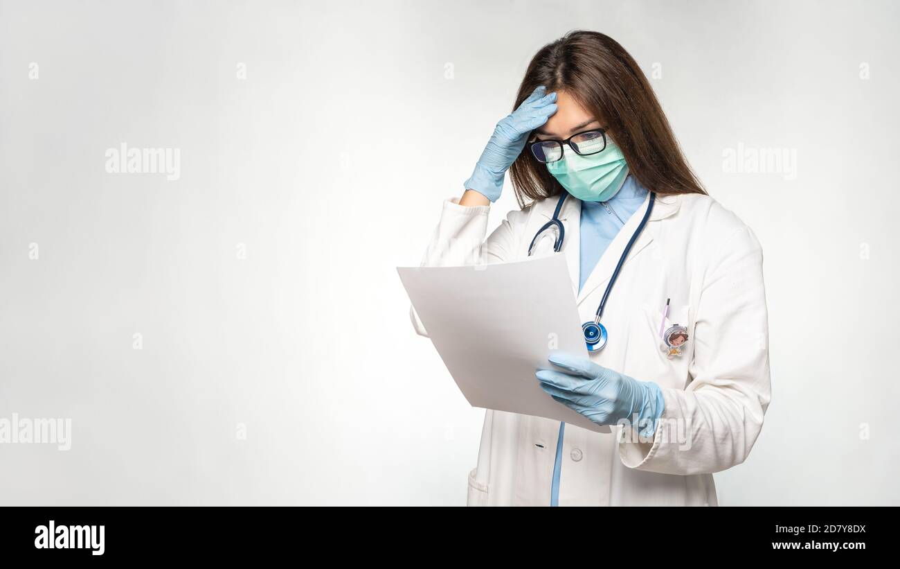 Young female caucasian doctor reading documents while holding her head. Medical record. Stock Photo