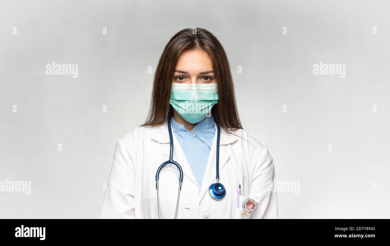 Female young doctor folded hands with protection medical mask, stethoscope over neck and white coat. Covid 19, coronavirus, healthcare concept banner. Stock Photo